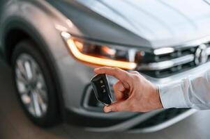 Keys, and remote controller. Close up view. Young man in white clothes is in the car dealership photo