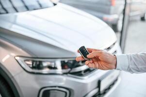Keys and remote ,controller. Close up view. Young man in white clothes is in the car dealership photo