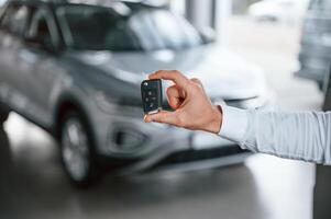 Close up view of keys that are in hand. Young ,man in white clothes is in the car dealership photo