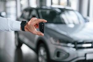 Close ,up, view of keys that are in hand. Young man in white clothes is in the car dealership photo