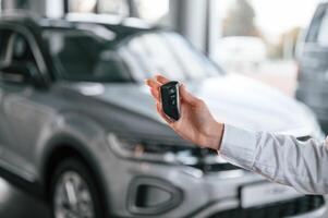 Close, up view of keys. Young ,woman in white formal clothes is in the at dealership photo