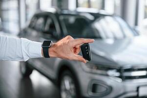 Close up view of keys that are in hand. Young man ,in white clothes is in the car dealership photo