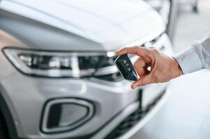 Keys ,and remote controller. Close up view. Young man in white clothes is in the car dealership photo
