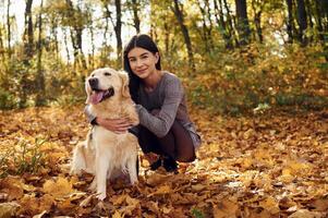 Sitting ,and, smiling. Woman is on the walk with her dog in the autumn forest at daytime photo