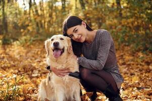 Sitting ,and smiling. Woman, is on the walk with her dog in the autumn forest at daytime photo