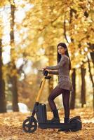 Standing, and posing. Young woman is riding electric scooter in the autumn forest photo