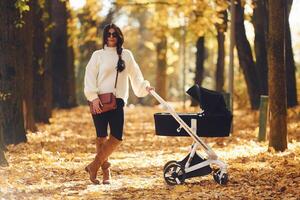 Mother with black, colored pram is having a walk in forest at daytime photo