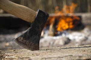 A sharp axe stands ready to chop logs next to a warm and inviting campfire in the woods. photo