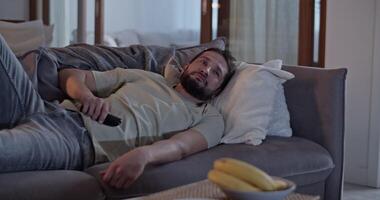 Sluggish man lying on sofa and using remote control video