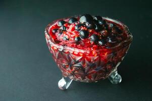 Raspberry and currant jam in a crystal vase on a dark background. Useful treat of dessert with vitamin C. Beautiful photos dessert in a transparent bowl. High quality photo
