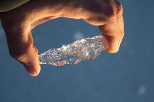 The large transparent crystal of ice in the human hand is seen in the sun's rays. Inside the crystal of interspersed and even rows of bubbles. Beautiful photos of crystalline objects. High quality