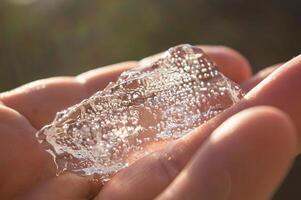 The large transparent crystal of ice in the human hand is seen in the sun's rays. Inside the crystal of interspersed and even rows of bubbles. Beautiful photos of crystalline objects. High quality