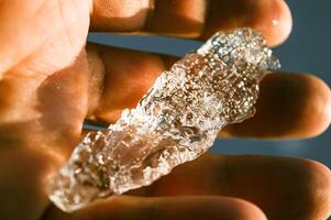 The large transparent crystal of ice in the human hand is seen in the sun's rays. Inside the crystal of interspersed and even rows of bubbles. Beautiful photos of crystalline objects. High quality