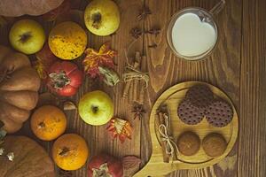 Cookies with milk on the table. Chocolate cookies and cinnamon on the wooden plate with a glass of milk and pumpkin with apple. photo