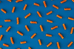 Trendy food pattern made of natural orange colored fusilli pasta on blue background. Minimal concept. Pasta aesthetic. Flat lay, top view. photo