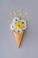 White and yellow flowers and petals in ice cream cone on grey background. Creative spring and summer concept. Flowers aesthetic. Flat lay style. photo