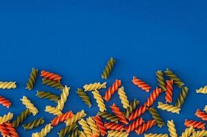 Colorful food layout with natural multicoloured fusilli on blue background with copy space. Minimal pasta concept. Creative food pattern backdrop. Pasta aesthetic. Flat lay style. Top view banner. photo
