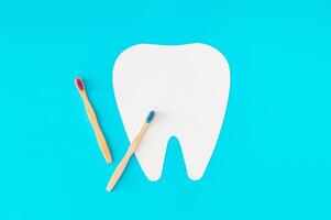 Creative layout with organic bamboo toothbrushes and white tooth shaped paper card note copy space on blue background. Minimal dental concept. Eco friendly, biodegradable and medical idea. Flat lay. photo