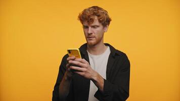 Surprised Red-Haired Man with Smartphone Against Yellow Background video
