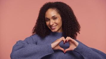Smiling woman making heart shape with hands on pink background video