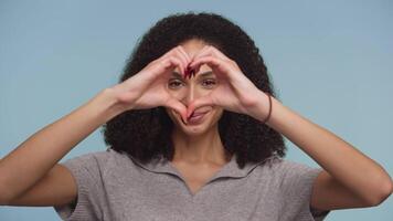 Smiling woman making a heart shape with hands on blue background video