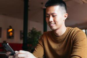 Smiling Asian man sitting in restaurant looking at smartphone. photo