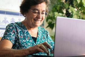 Senior woman with glasses using a laptop and a notebook at home photo