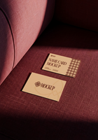 Two beige name card mockups rest on a burgundy fabric surface psd
