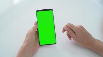 fêmea mãos usando Smartphone com verde tela chromakey em branco mesa, tocando tela sensível ao toque e interagindo com Móvel dispositivo, conceito do digital tecnologia, conectados comunicação, aplicativo costumização video