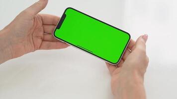 Women's Hands Holding Smartphone With Green Chroma Key Screen, Horizontal Display for Mockup or Replacement in Neutral Studio Light, Game Movement video