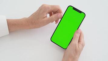 Woman's hands navigate smartphone boasting striking green screen for creative design applications. Touch and scrolling movements show involved in digital interaction on minimalist white background. video