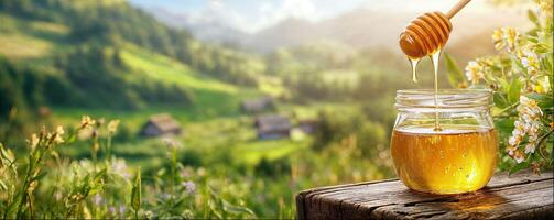 Honey pouring from honey dipper into jar, close-up, sunny landscape with flower meadows, copy space photo