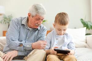 Happy family at home. Old senior man grandfather boy grandson enjoying time together watching on phone. Good time at home. grandparent and child together. Older generation modern tech usage photo