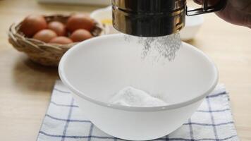 Close up of a person sifting flour into a white mixing bowl while preparing ingredients for baking A basket of fresh brown eggs and a small bowl video