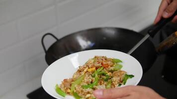 person serving freshly cooked fried rice with vegetables, including green beans and red bell peppers, from a wok onto a white plate using a metal spatula in a home kitchen setting video