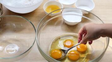 Cracking and Separating Eggs in Glass Bowl for Baking Preparing Cake Batter with Flour Sugar and Butter on Wooden Kitchen Counter with Ingredients in Small Bowls for Homemade Dessert video