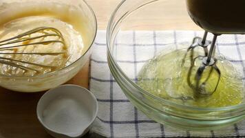 Whisking Egg Whites with Hand Mixer While Preparing Cake Batter Baking Process with Sugar and Creamy Mixture in Glass Bowls on Kitchen Counter video