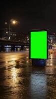 A green screen billboard stands on a wet city street at night with bridge and lights visible afar video