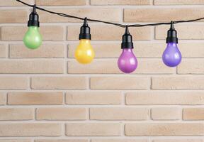 Colorful light bulbs hanging from a string on a brick wall photo
