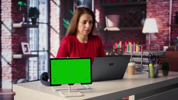 Mature woman reading forms and papers next to isolated screen and studying handwritten notes, surfing the web and staying connected for her freelance work tasks. Multitasking online. Camera B. video