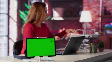 Freelancer does research by reading articles and papers next to chroma key display, collecting information for new project. Woman multitasking and studying files with handwritten notes. Camera A. video