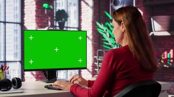 Adult woman typing on pc with chroma key screen at her loft desk, engaging in online work, multitasking efficiently and embracing the flexibility of remote tasks in a home setting. Camera A. video