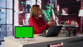 Freelancer does research by reading articles and papers next to chroma key display, collecting information for new project. Woman multitasking and studying files with handwritten notes. Camera B. video