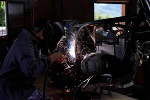 Anonymous workman using welding machine while fixing motorbike i photo
