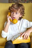 Pensive boy talking on retro telephone in room photo