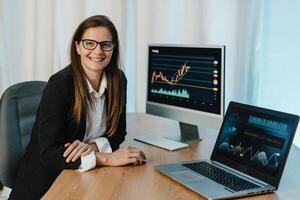Female trader at table with laptop and computer monitor photo