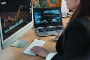 Crop trader at table with laptop and computer screen photo