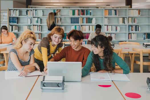 Happy diverse groupmates using laptop and smiling while doing task in library photo