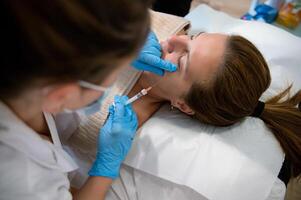 Cosmetologist administering injection in face of client during rejuvenation treatment in hospital photo