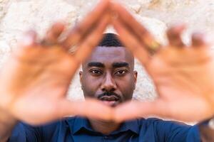 Black man showing triangle gesture with hands near wall photo